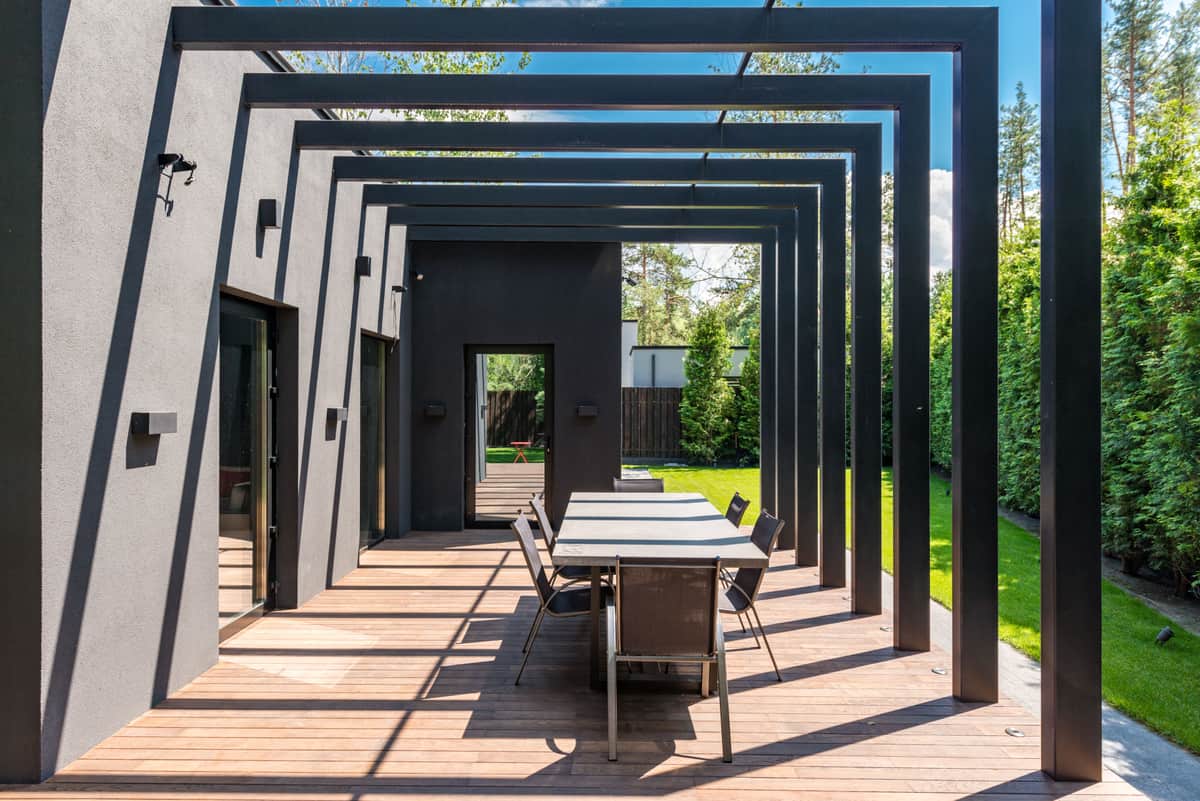 Aluminum louvered pergola over a paved backyard patio in flat daylight, louvers part open